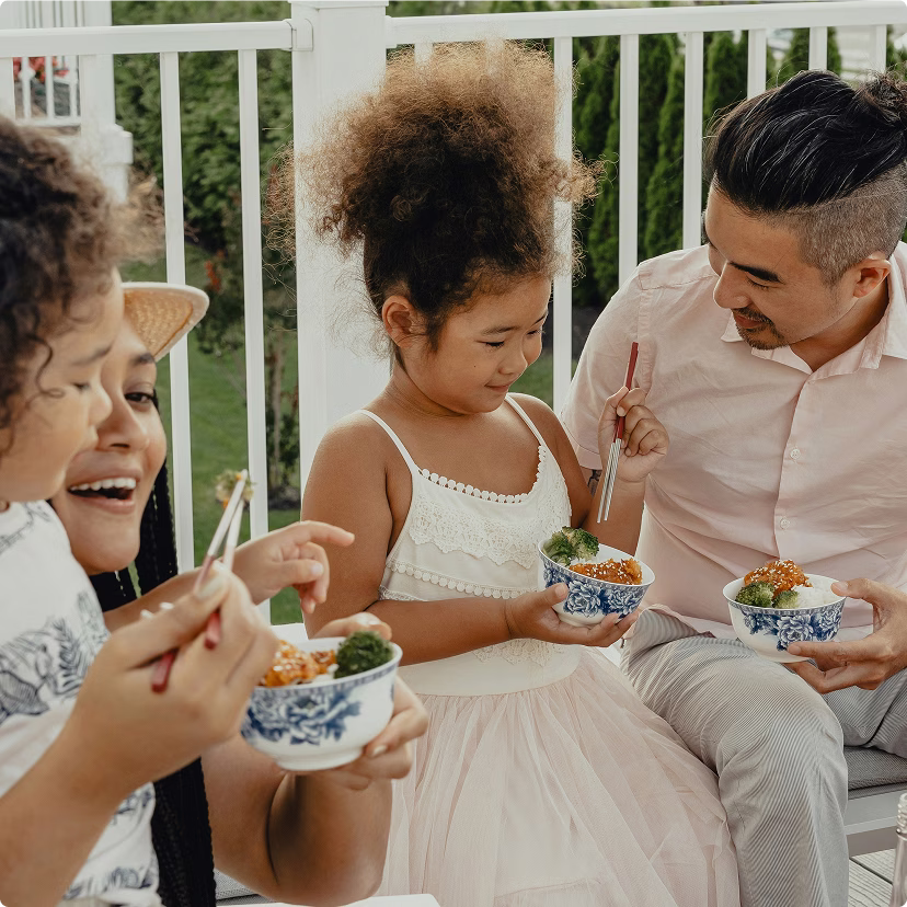 Family of four, sitting outside on their patio, having a meal together.