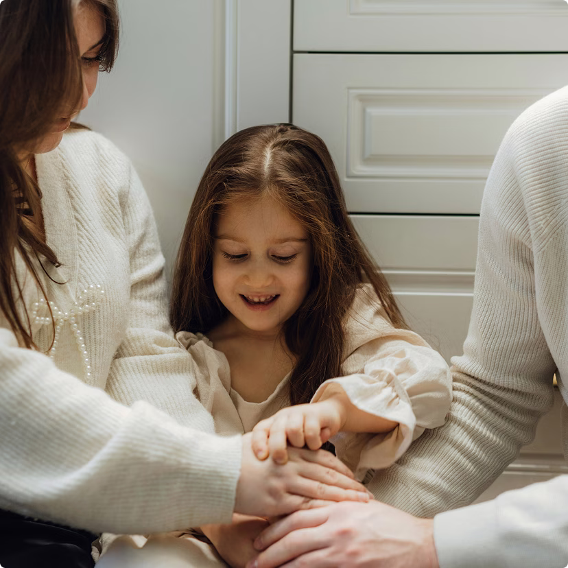 Young child and parents stacking hands, while sitting on the floor.