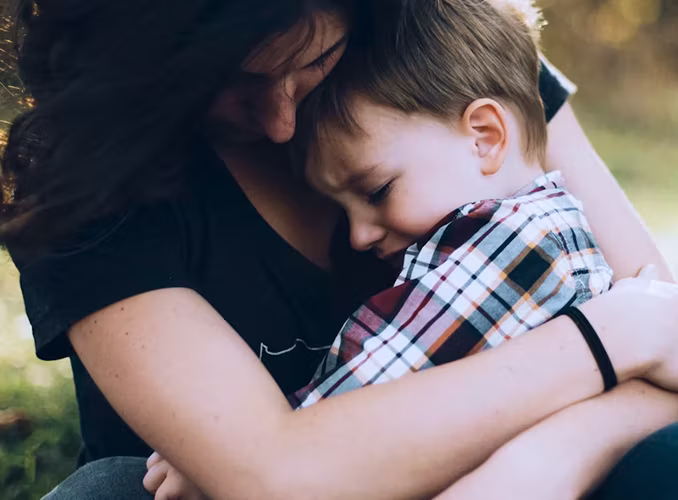 A woman holding a young boy closely in a gentle embrace outdoors.