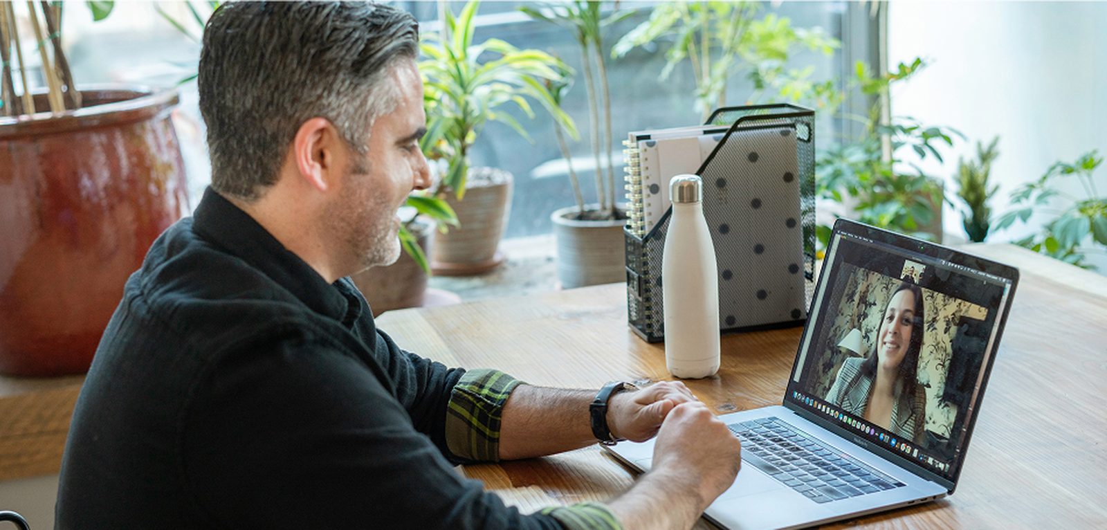 A man smiling during a video call with a woman visible on his laptop screen.